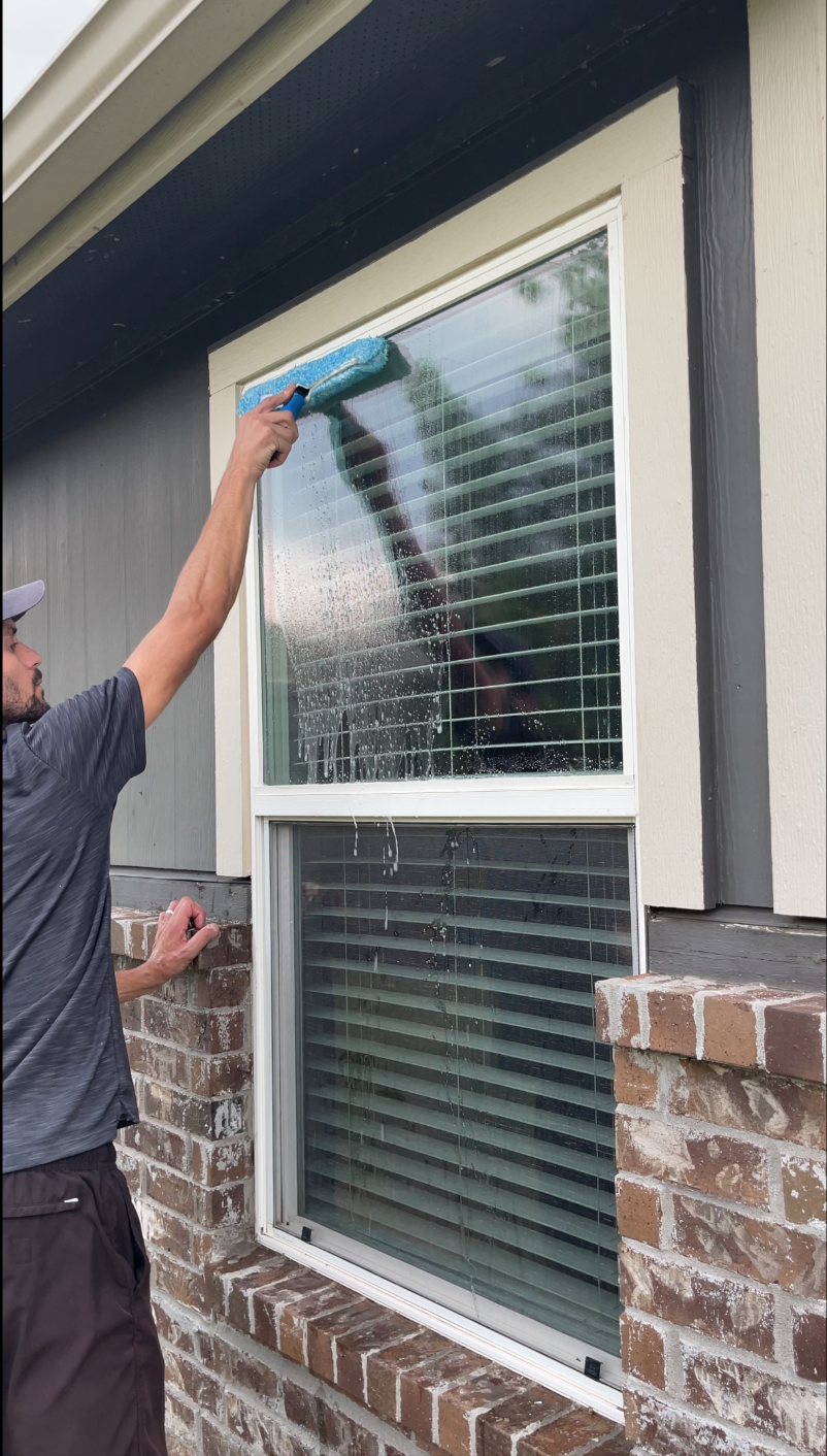 Cleaning a high second-story window with a water-fed pole