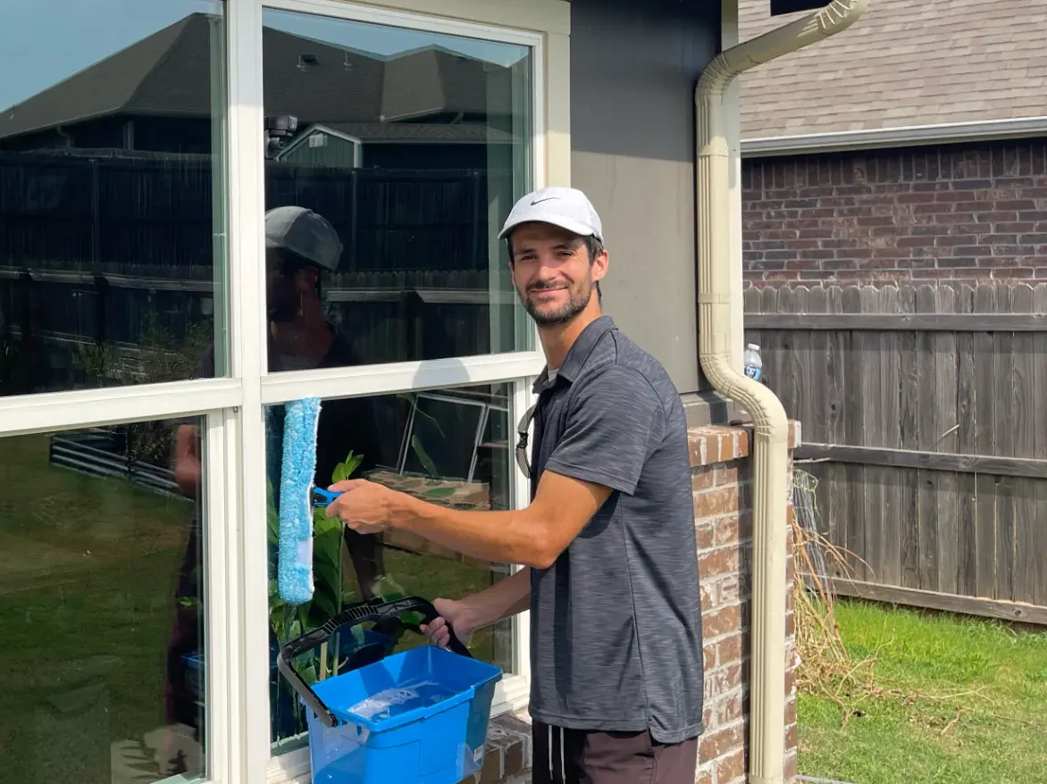 Austin smiling while cleaning a residential window in Broken Arrow